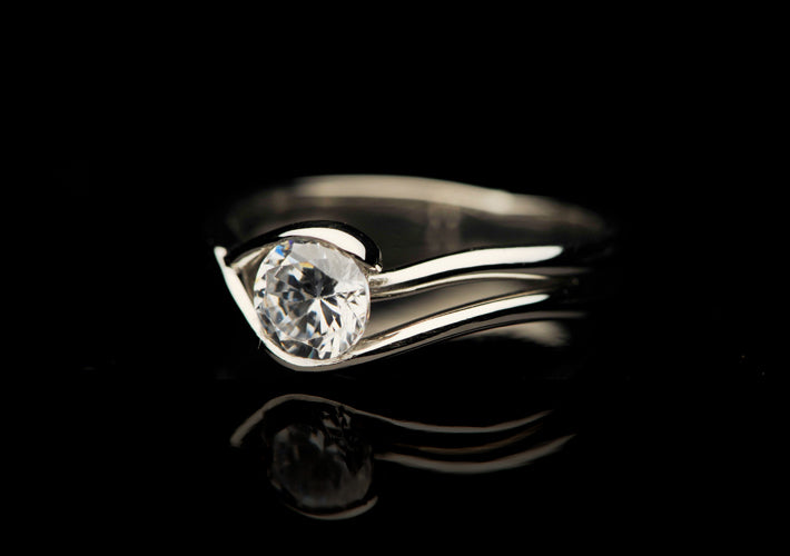 A sculptural platinum and diamond ring on a black background